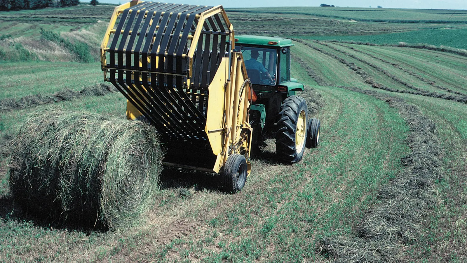 A tractor and round baler making hay in Iowa