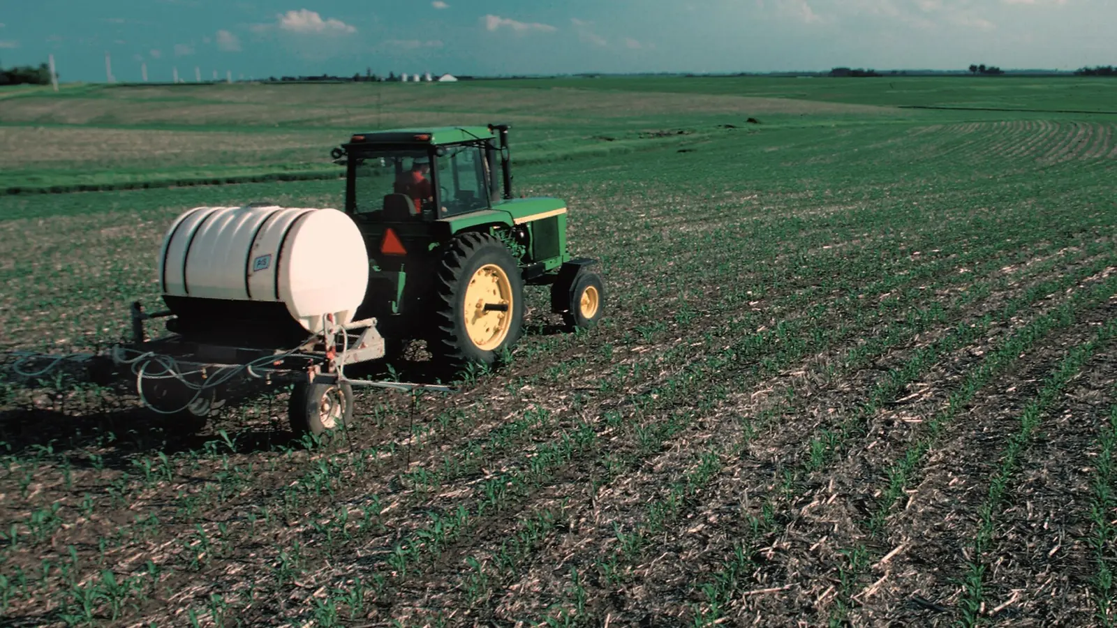 A tractor applying fertilizer to a young corn field in Iowa